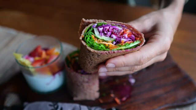 Appetizing vegetarian rolls wrapped in flatbread filled with various vegetables. On a wooden plate, a healthy breakfast of a vegetable dish and a drink with fruits and berries. Delicious vegan.