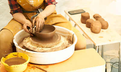 A Potter works with red clay on a Potter's wheel in the workshop..Women's hands create a pot. Girl sculpts in clay pot closeup. Modeling clay close-up. 