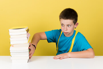 Cute schoolboy rejecting to study isolated on yellow background. Student boy moving away pile of books.