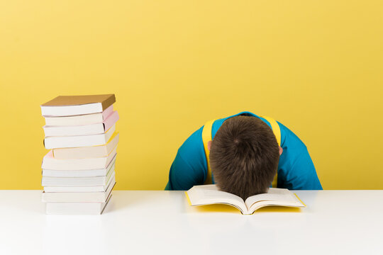 Stressed boy sleeping with head on table.  Overwhelmed student isolated on yellow background.