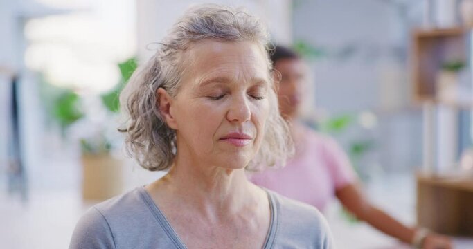 Mature woman meditating with eyes closed during a group fitness class in a yoga studio. Face of a calm, relaxed and focused senior lady sitting and praying quietly for inner peace and zen energy