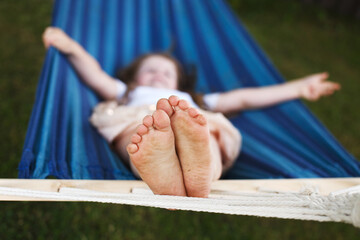 closeup of little girl's feet relaxing in the blue hammock during her summer vacation in back yard