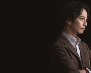 スーツを着て腕組みをしている日本人男性ポートレート、スタジオ撮影黒背景横向き
