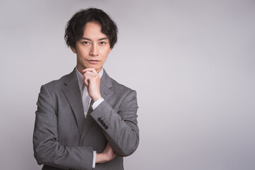 グレーのスーツを着た男性が顎に手をあてている/ビジネスパーソン