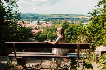 A woman sits with her back on a bench and looks at the city and the mountains