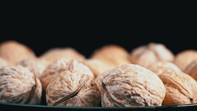 Lot of walnuts in the shell are spinning on a black background. Nuts are good for the brain. Heap of walnuts close-up.