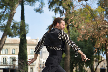 Young man with beard and ponytail, wearing black shirt with white polka dots and black pants and...