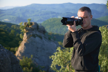 Nature photographer with digital camera on top of the mountain in the morning, taking photo of sunset mountains. Concept of travel lifestyle.