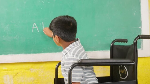 Young teenger school kid with disability on wheel chair writing on board while looking at camera - concept of education, growth and development