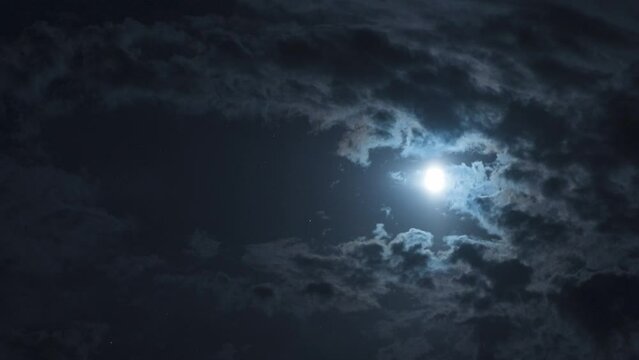 Mysterious night sky with full dramatic moon clouds in moonlight. Nighttime timelapse. The movement of clouds and the moon across the night sky