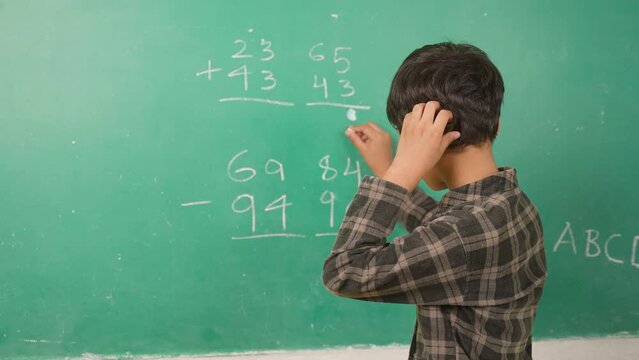 Confused kid scratching head to solve mathematics problem on board at classroom - concept of intelligence, trouble learning and education