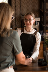 Young smiling woman salesperson give away order to female client in coffee shop
