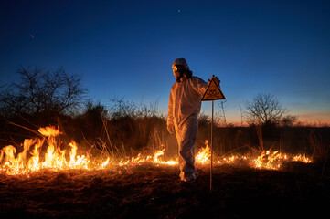 Firefighter ecologist extinguishing fire in field at night. Man in protective suit and gas mask...