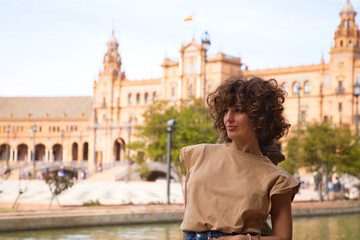 beautiful woman with curly hair is on holiday in sevilla. The woman is posing for pictures in front of the most famous square of the centuries old city. Holiday and travel concept.