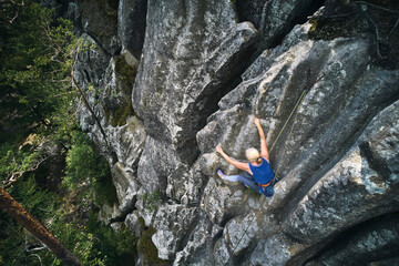 Senior alult woman climbing difficult route on a high rock with rope. Fearless climber training...