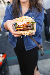 A view of a person holding out a ramen burger.