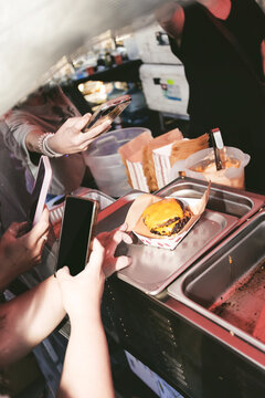  A view of several people using their smart phones to take a photo of a cheeseburger, seen at a local food festival.