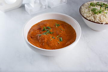 A view of a bowl of butter chicken, with a bowl of basmati rice.