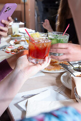 A view of some hands holding cocktails, in the middle of a drink cheers.