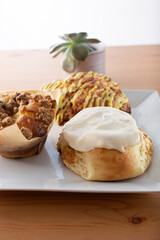A view of several breakfast pastries on a plate, featuring a blueberry muffin, cinnamon roll and a scone.