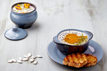 Pumpkin cream soup with cream, black cumin seeds, herbs and toasted bread on a light blue wooden table