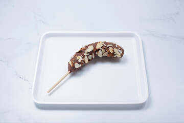 A view of a frozen chocolate covered banana, with almond slice toppings.