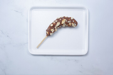 A top down view of a frozen chocolate covered banana, with almond slice toppings.