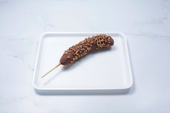 A View Of A Chocolate Covered Frozen Banana With Crushed Almond Toppings.