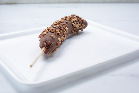 A View Of A Chocolate Covered Frozen Banana With Crushed Almond Toppings.