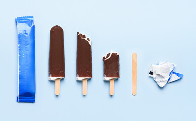 Chocolate covered ice cream on wooden stick at different states of consumption life cycle on blue background top view flat lay
