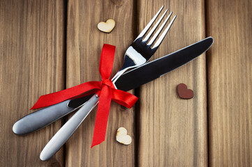 A set of fork and knife tied with a red ribbon on a wooden table.