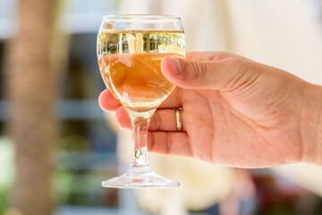 A full glass of white wine in a man's hand.
