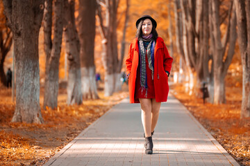 Elegant beautiful adult woman in a red coat and hat walks along the path of the autumn Park