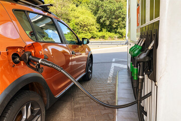 Pumping gasoline fuel in orange car at a gas station. Fill car with fuel in petrol station. Close up.