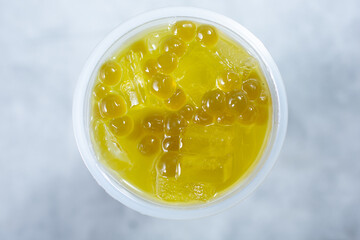 A top down view of yellow green colored fruit tea, in a plastic cup.