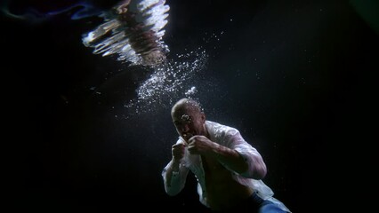 a man in an unbuttoned white shirt fights with a shadow in dark water with bubbles and is reflected in the surface. the camera is tilted
