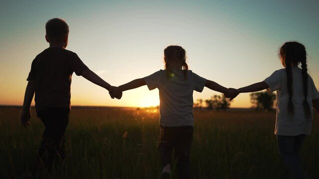 Happy family. Silhouette of a family on walk. Group of children walk on grass in the park. Children holding hands walk in park at sunset. Silhouette of children walk in nature. Happy family concept