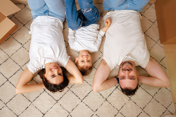 Happy family lying on the floor in new home with cordboard boxes around