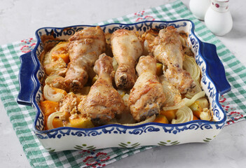 Baked chicken drumsticks with pumpkin and potatoes in ceramic form on light background