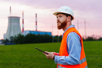 An engineer with a tablet on the background of a power plant. Inspection of engineering systems. A man in a helmet and an orange vest