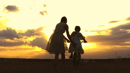 silhouette child bike. mother teaches little child ride bike sunset. happy family. chidhood dream. real lesson sport learning ride wheels. silhouette kid girl with mom park. health fun family trip