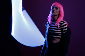 Portrait of female model posing with fluorescent neon light, holding violet purple color lights...