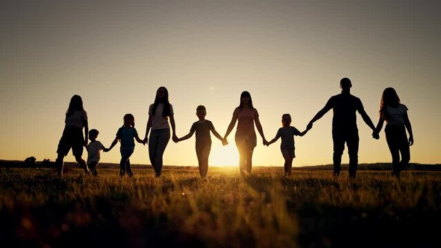 Happy family. Silhouette of large group of people at picnic in park. The family generation walks on the green grass. Parents and children play in nature. Family walking together across field at sunset