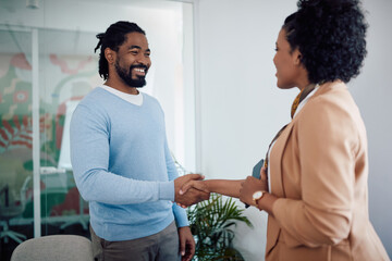 Happy African American man handshaking with female member of human resource team after job interview in office.