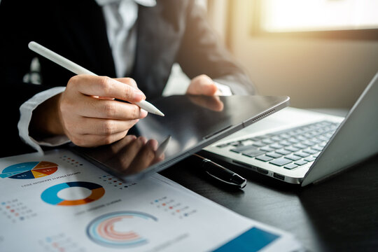Close up of Businesswomen or Accountant using a digital tablet and laptop computer with analyzing business report graph and finance chart at the workplace, financial and investment concept.