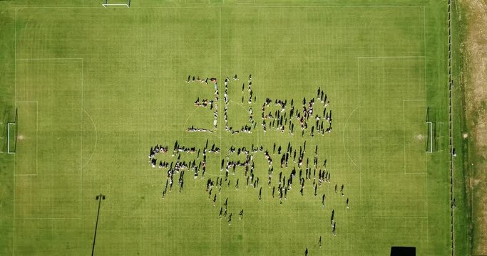 People Forming 30 ANS On The Grassy Field During 30th Year Anniversary Of Sports Association. aerial top-down