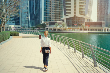 Back view of young woman walking on city embankment.