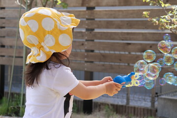 庭でシャボン玉を楽しむ帽子をかぶった小さな女の子