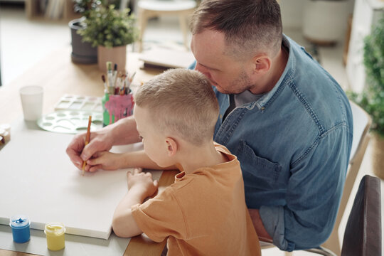 Father teaching his son to paint a picture at table during their leisure time