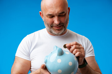 Middle-aged man holding piggy bank against blue background